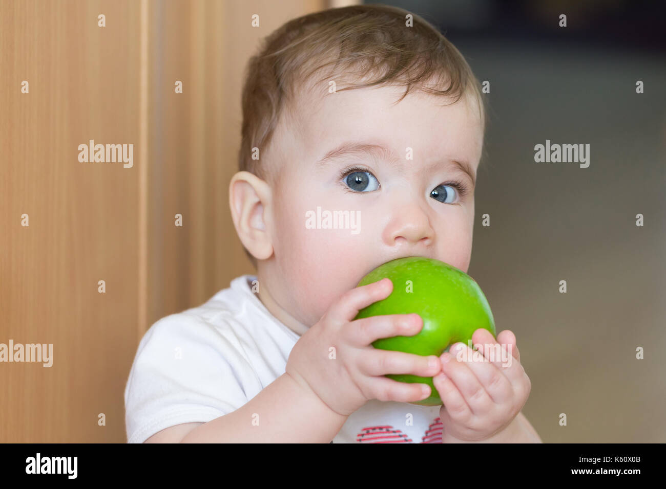 Small child with a big green apple. A child bites an apple with a surprised look. Stock Photo