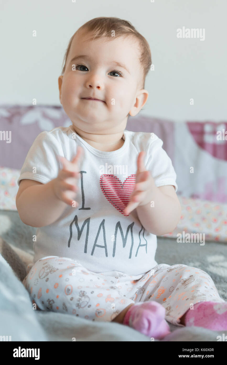 Vertical shot. Little baby smiling sits on bed at home. Stock Photo