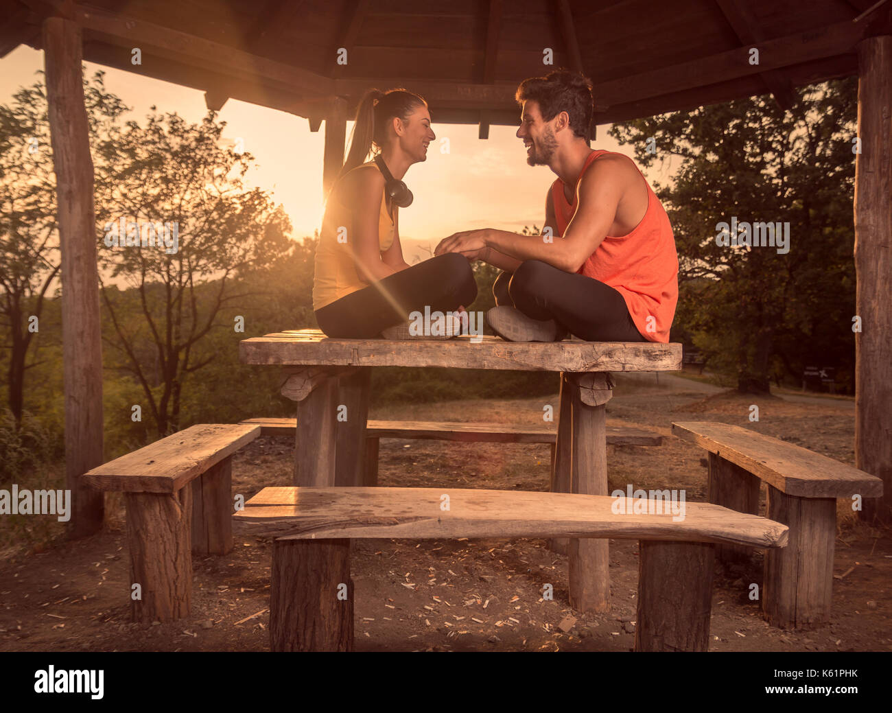 two people, young couple, smiling, sitting on wood table, outdoors, warm sunny day Sun, relaxing, sport clothes Stock Photo