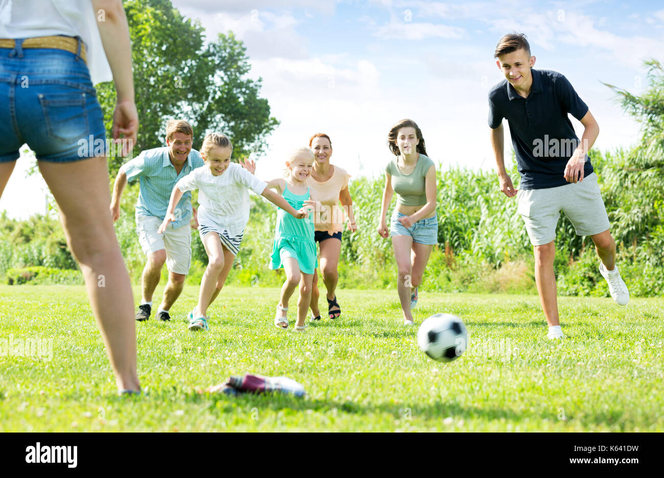 Parents with four smiling kids playing soccer together on green field ...
