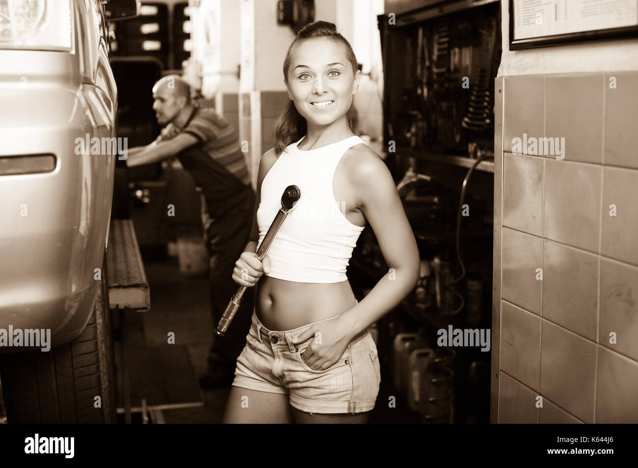 Happy mechanic woman working on car wheel in service point Stock Photo
