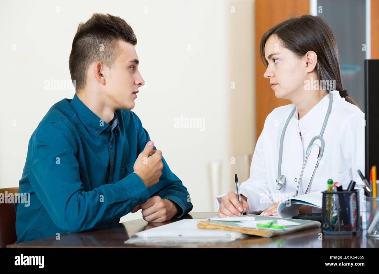 Female spanish doctor receiving and questioning teen patient at office