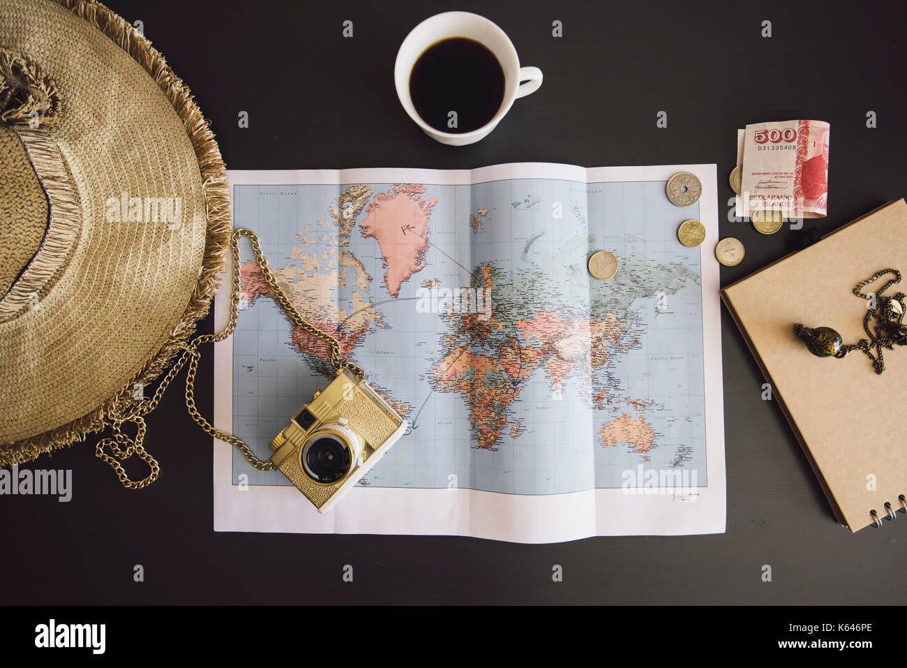 Planning the trip. World map with the hat, film camera, some money, notebook from recycled paper and freshly brewed coffee cup on the dark table Stock Photo