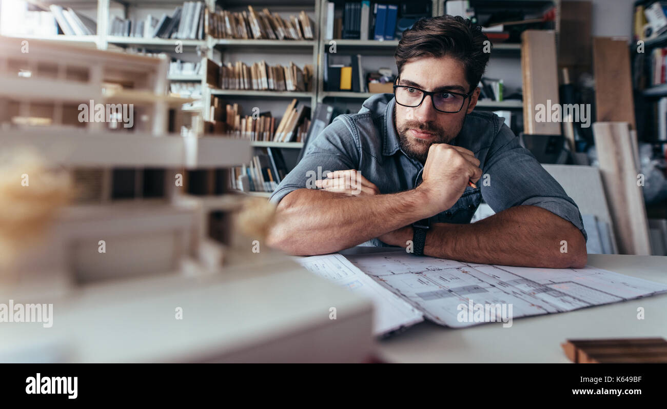 Architect looking at house model and thinking. Creative designer sitting in office and working on new project. Stock Photo