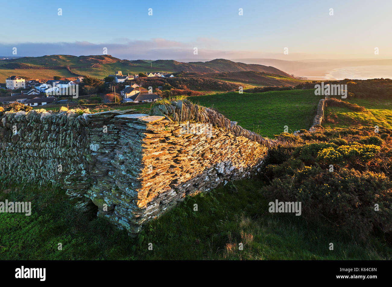 Corner of a dry stone wall in a North Devon field with views of Mortehoe village  and Woolacombe bay in the background Stock Photo