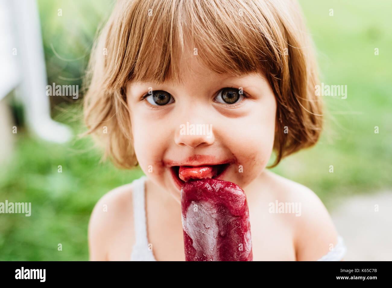 A little girl eats a grape ice lolly, ice pop popsicle. Stock Photo