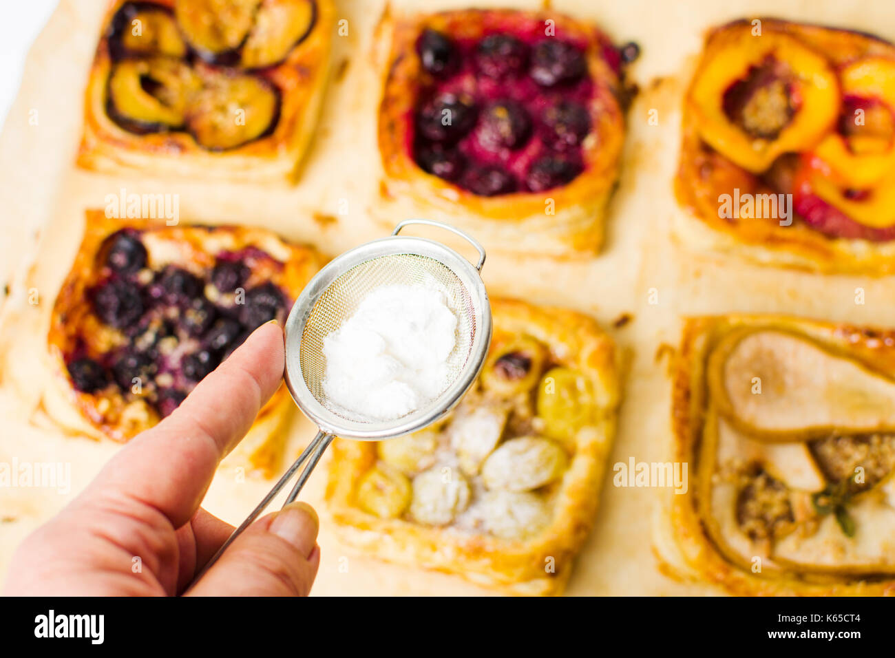 Adding sugar to fruit sweet pie slices on baking paper Stock Photo