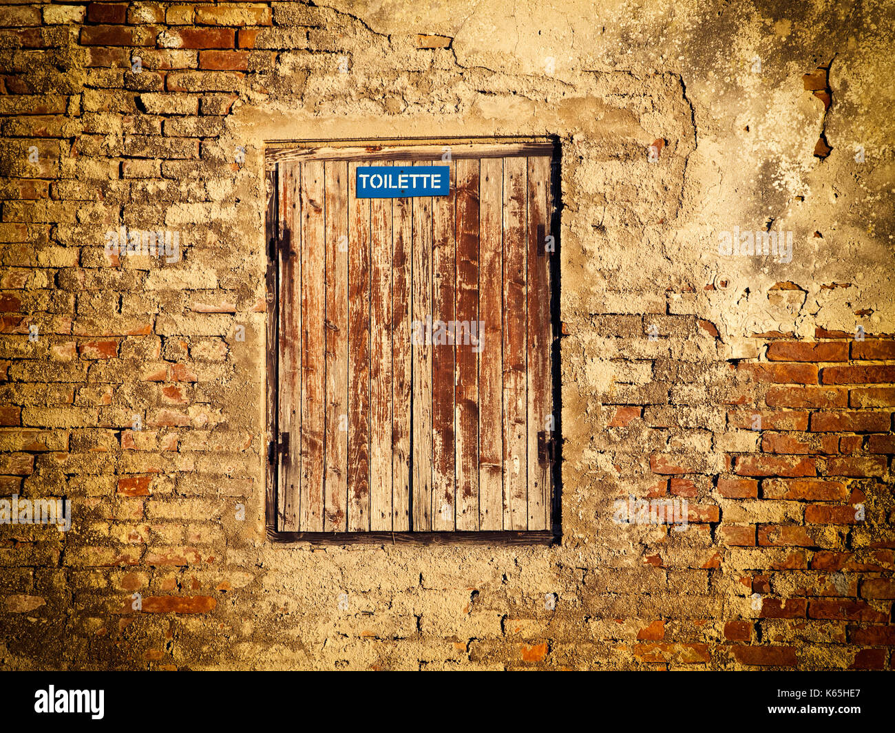 Old brick wall with an old window and toilette sign. Stock Photo