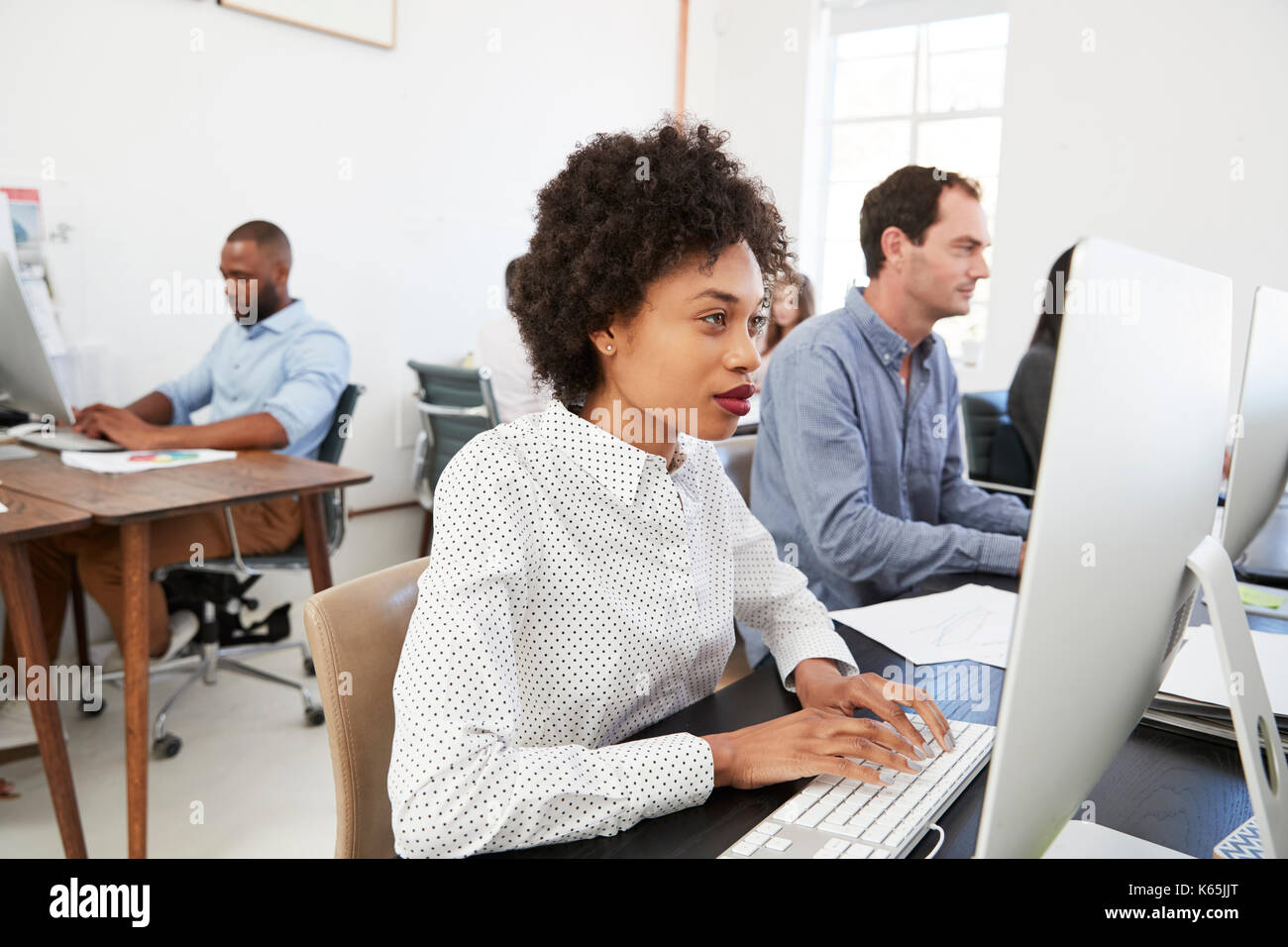 Young woman at computer with colleagues in open plan office Stock Photo