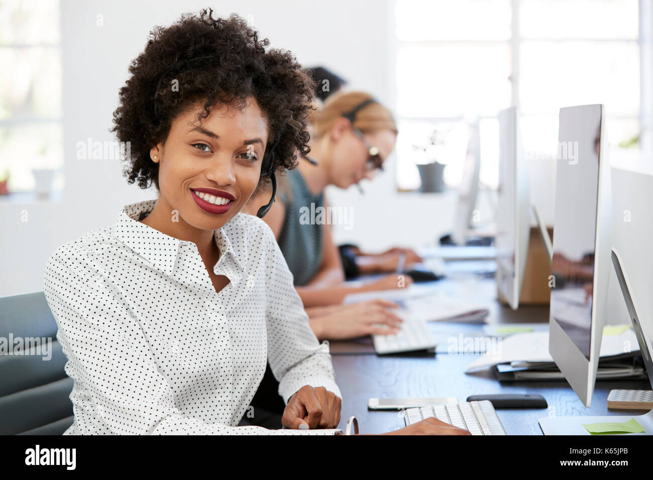 Young black woman with headset smiling to camera in office Stock Photo ...