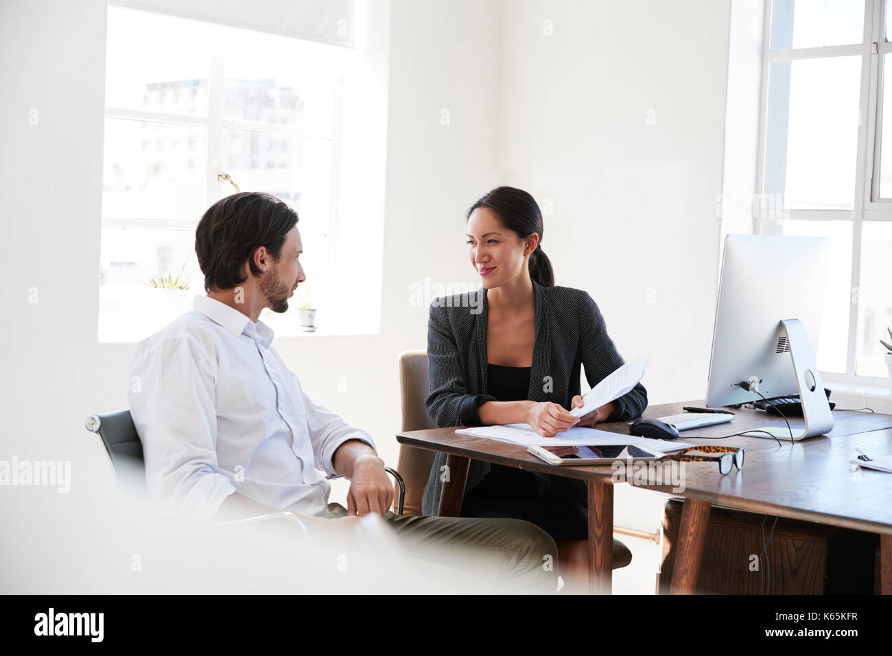 Man and woman discussing documents at a desk in an office Stock Photo ...