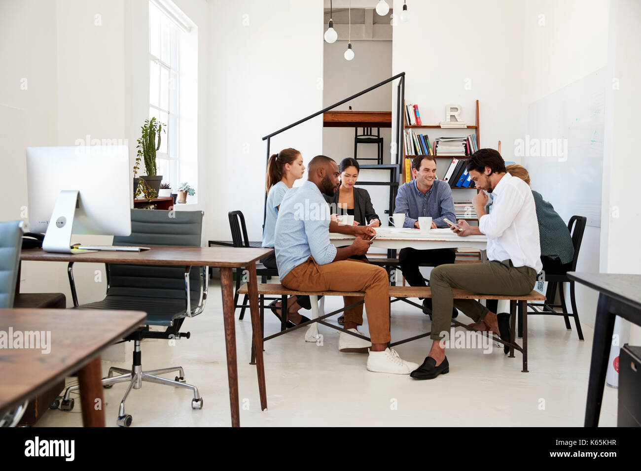 Creative team meet at a table in an office, one using phone Stock Photo