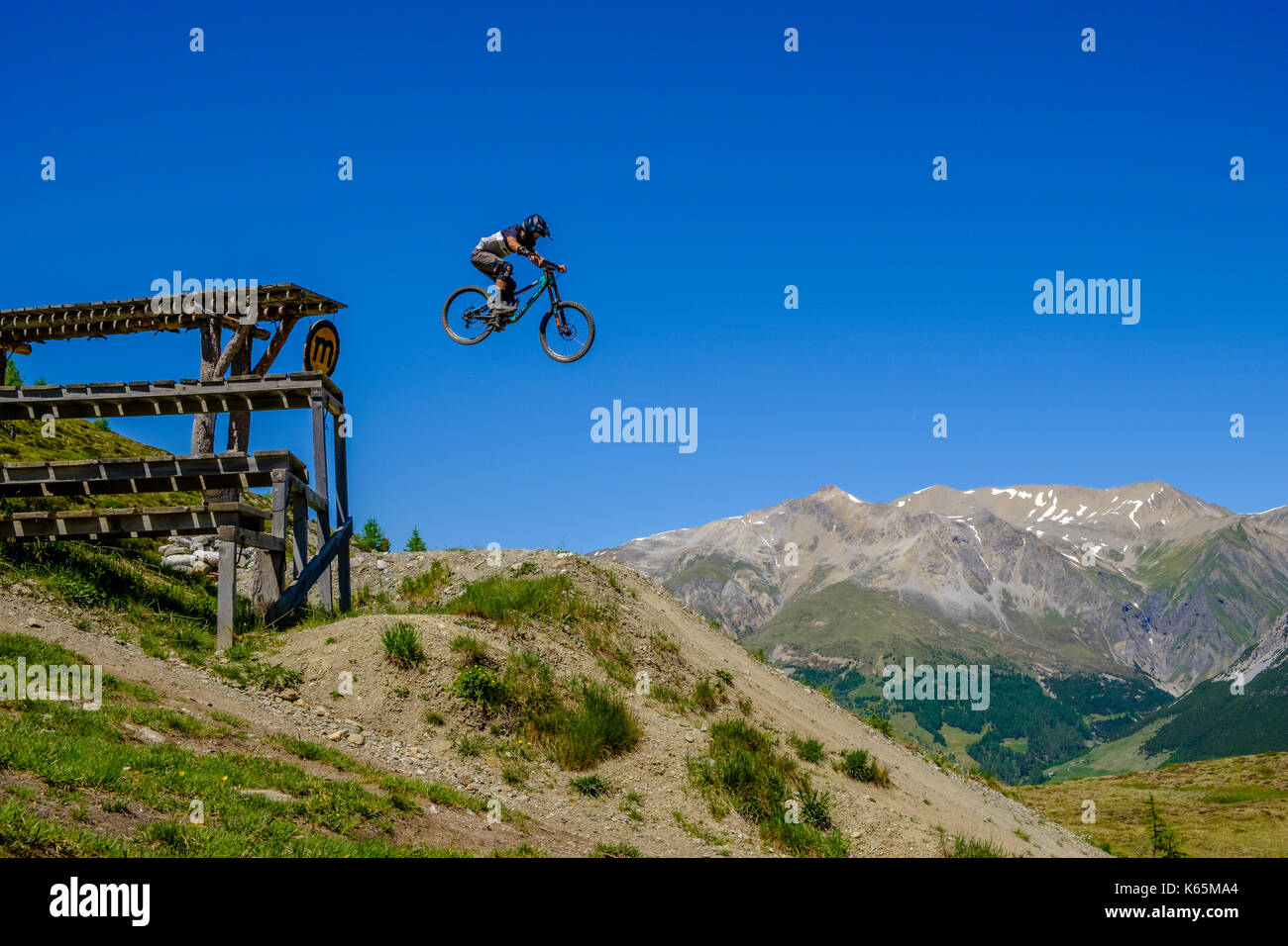 Downhill cyclist in action jumping down from a platform in the Motolino Bike Park Stock Photo