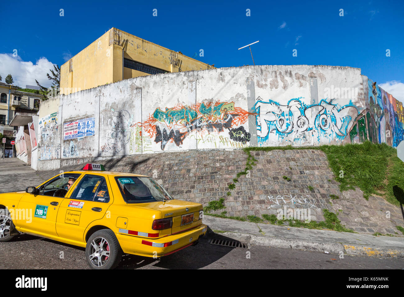 Yellow taxi cab and roadside urban art and grafitti on a wall in the suburbs of Quito, capital city of Ecuador, South America, a typical street scene Stock Photo