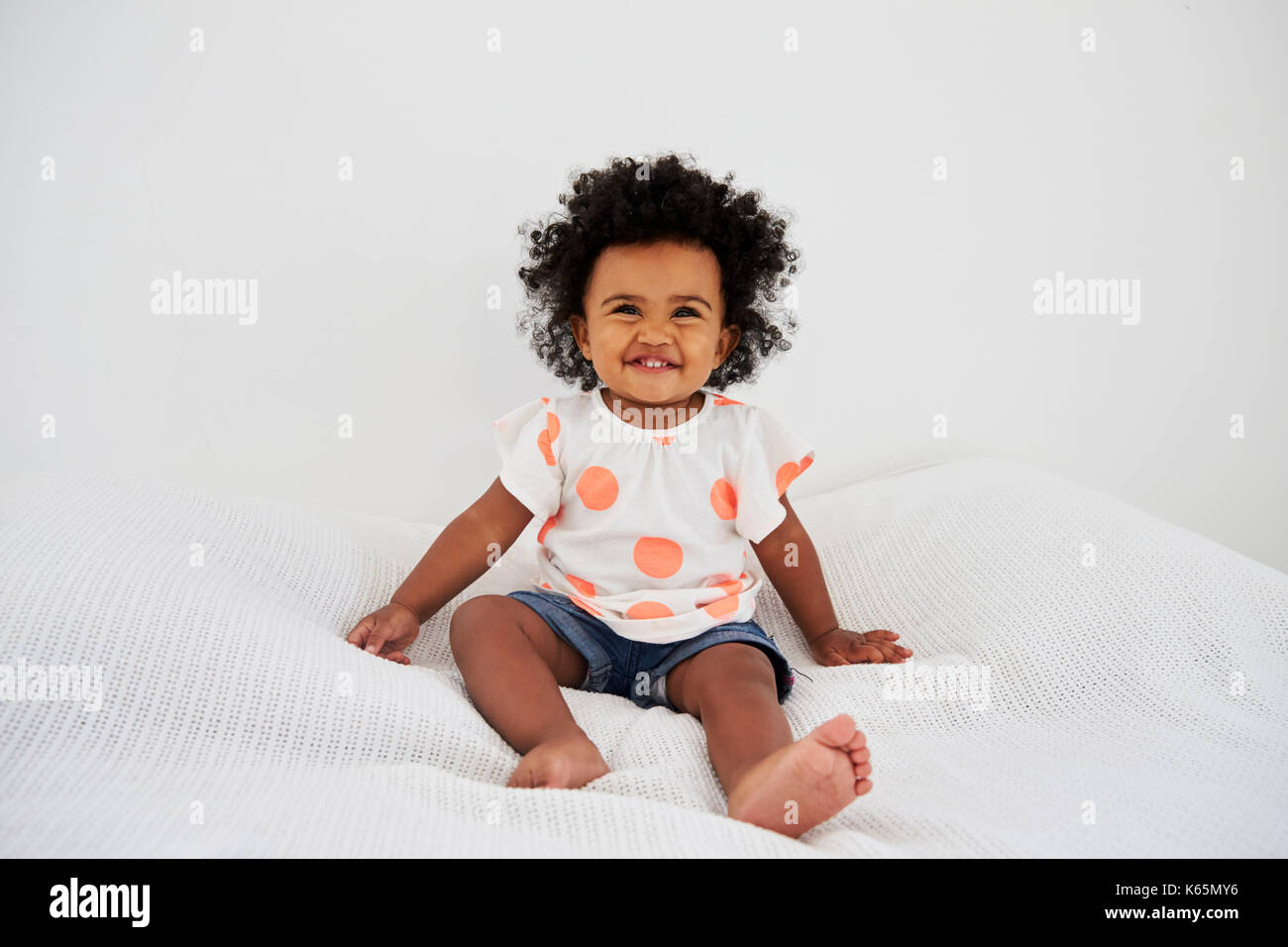 Portrait Of Smiling Baby Girl Sitting On Bed Stock Photo - Alamy