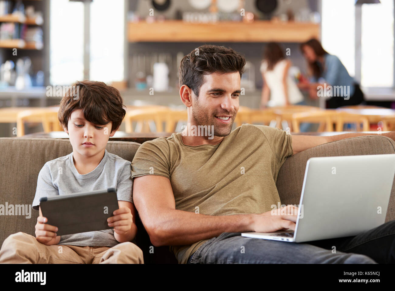 Father And Son Sitting On Lounge Sofa Using Digital Devices Stock Photo