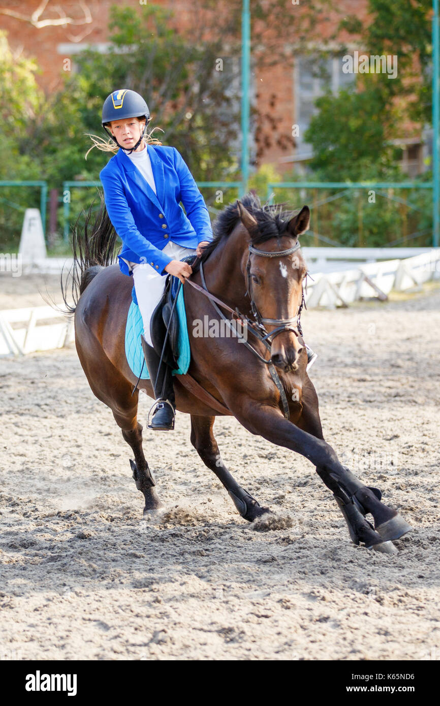Young girl on bay horse galloping on her course on show jumping competition Stock Photo