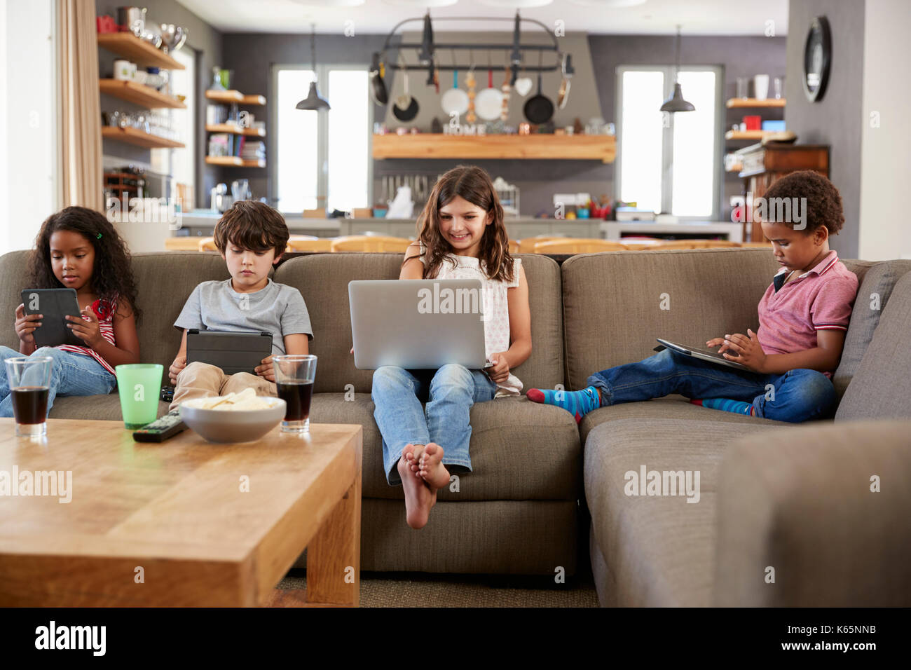 Group Of Children Sitting On Sofa Using Digital Devices Stock Photo