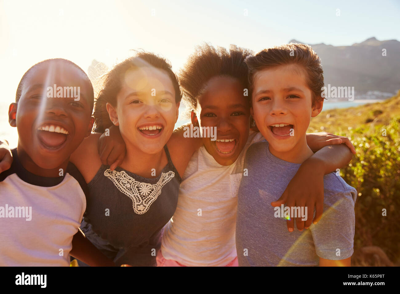 Portrait Of Smiling Children Standing On Cliffs By Sea Stock Photo