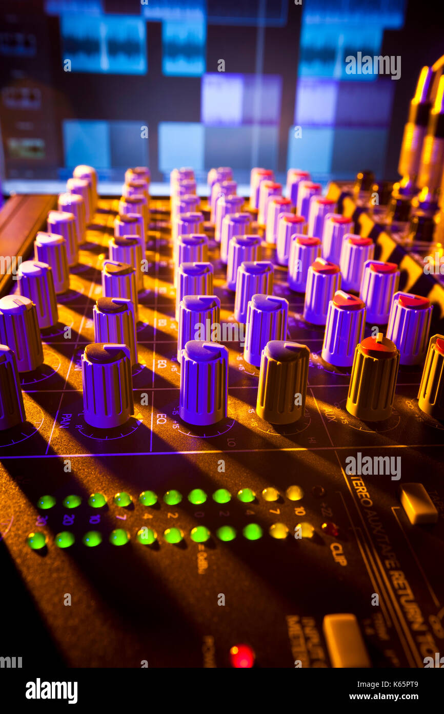 Close-up of audio mixing desk with background computer screen. Selective focus on foreground controls Stock Photo