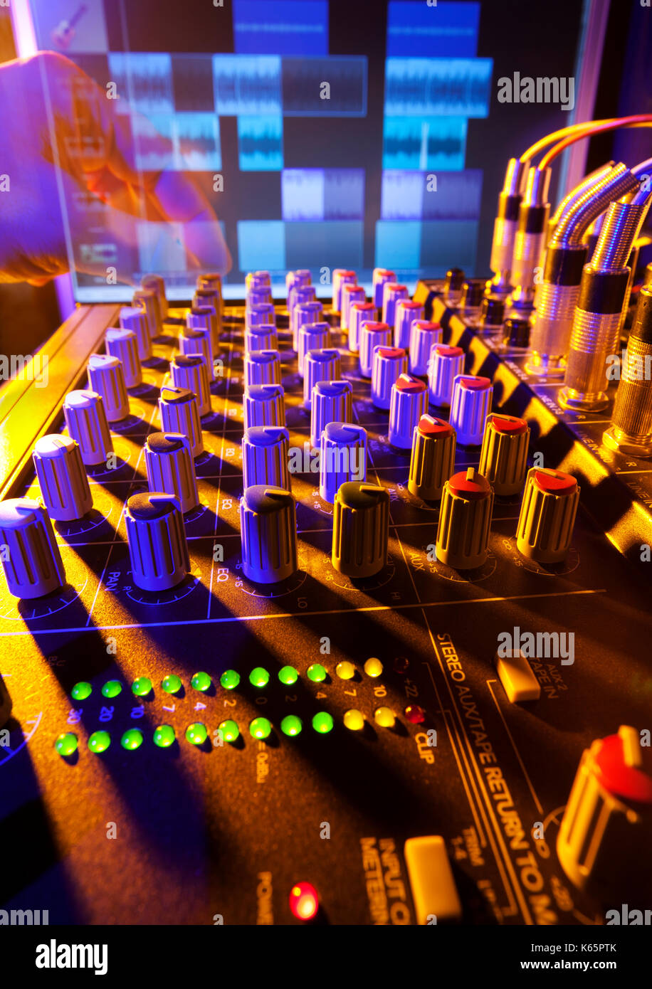 Close-up of an audio mixing desk with background computer screen. Motion blurred hand on distant controls. Selective focus on mixer controls Stock Photo