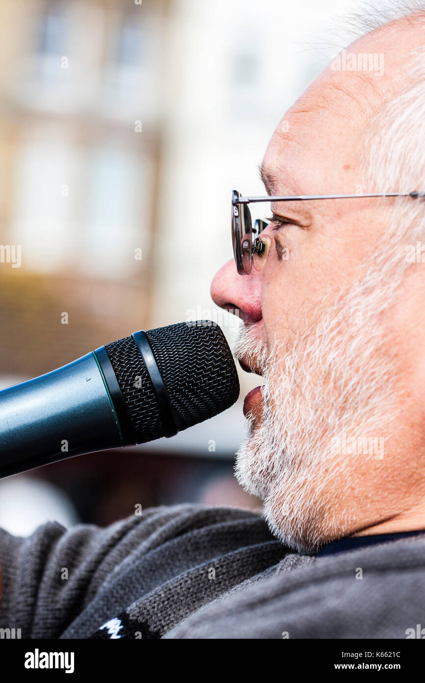 Mick Scott, presenter at Broadstairs Folk Week. Portrait of face, side view, white stubble and wears sunglasses. talking into microphone. Stock Photo