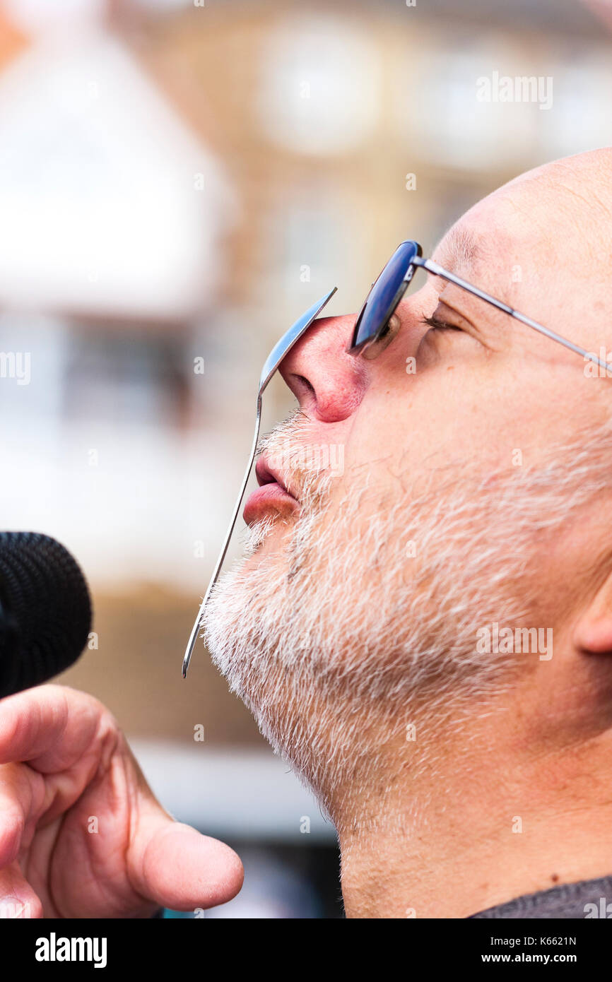 Mick Scott, presenter at Broadstairs Folk Week. Portrait of face, side view, balancing spoon on nose, white stubble and wears sunglasses. Stock Photo