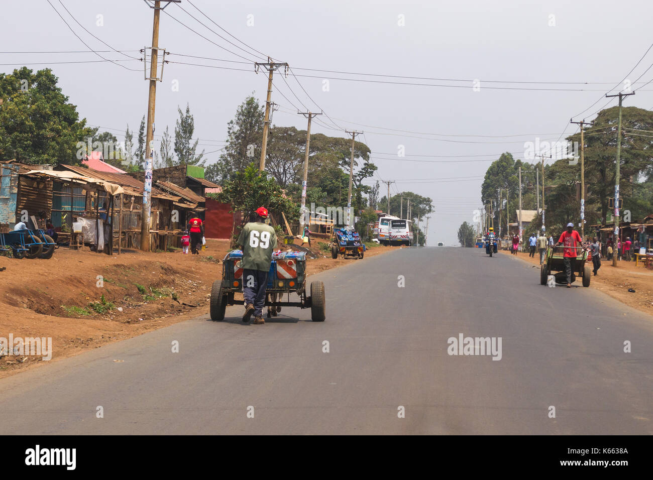 Men pushing carts with water containers down main road of a town, Kenya Stock Photo