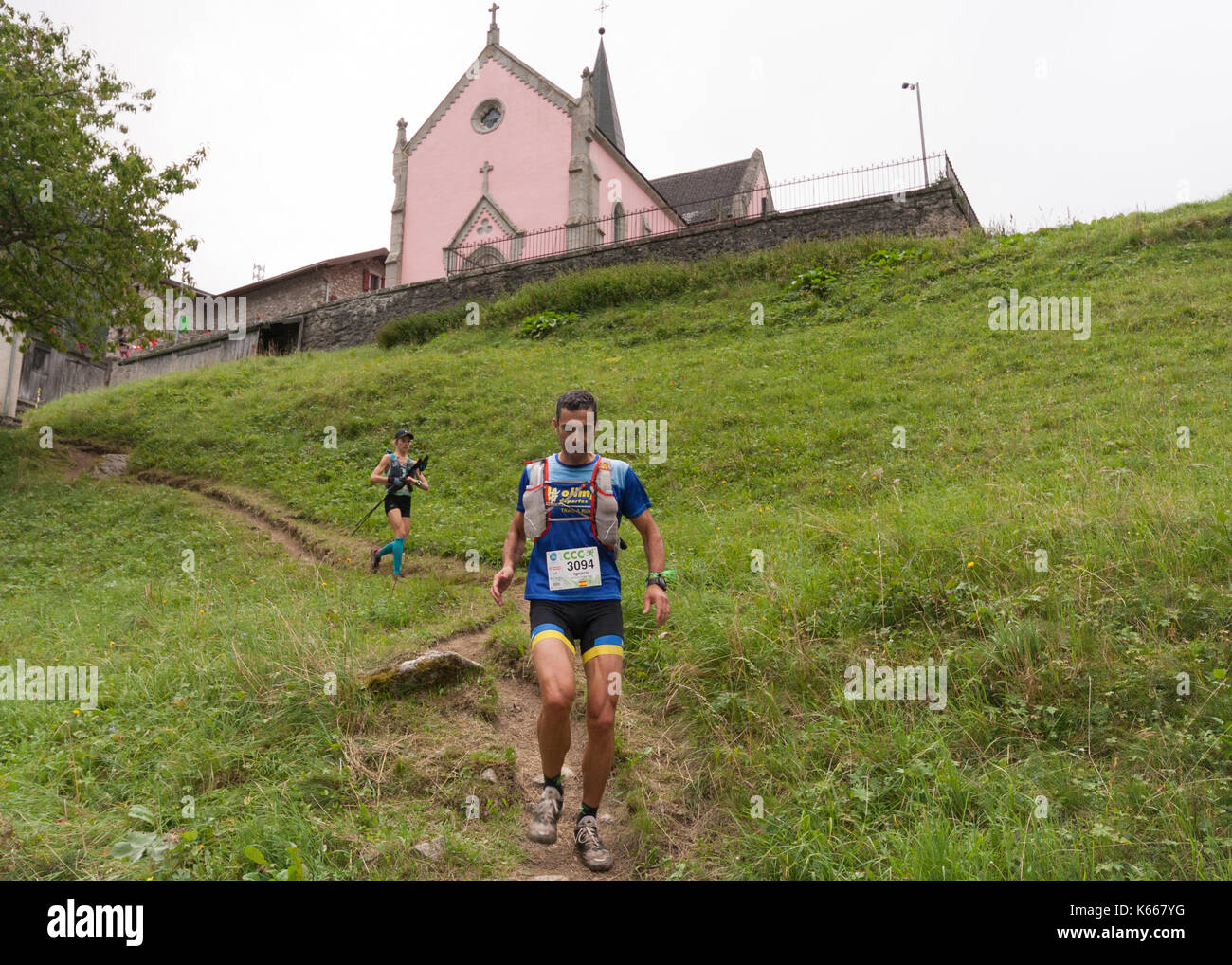 Two runners in the 2017 CCC Courmayeur-Champex-Chamonix endurance race pass under the church in the village of Trient in Switzerland. Stock Photo