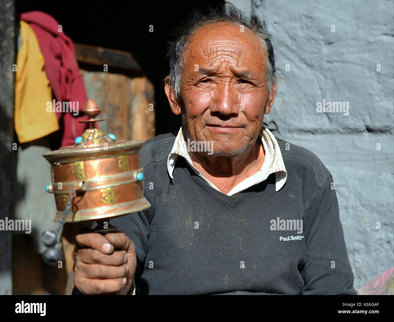 Old Nepali Gurung man swings a Tibetan hand prayer wheel (mani wheel) with his right hand and poses for the camera. Stock Photo