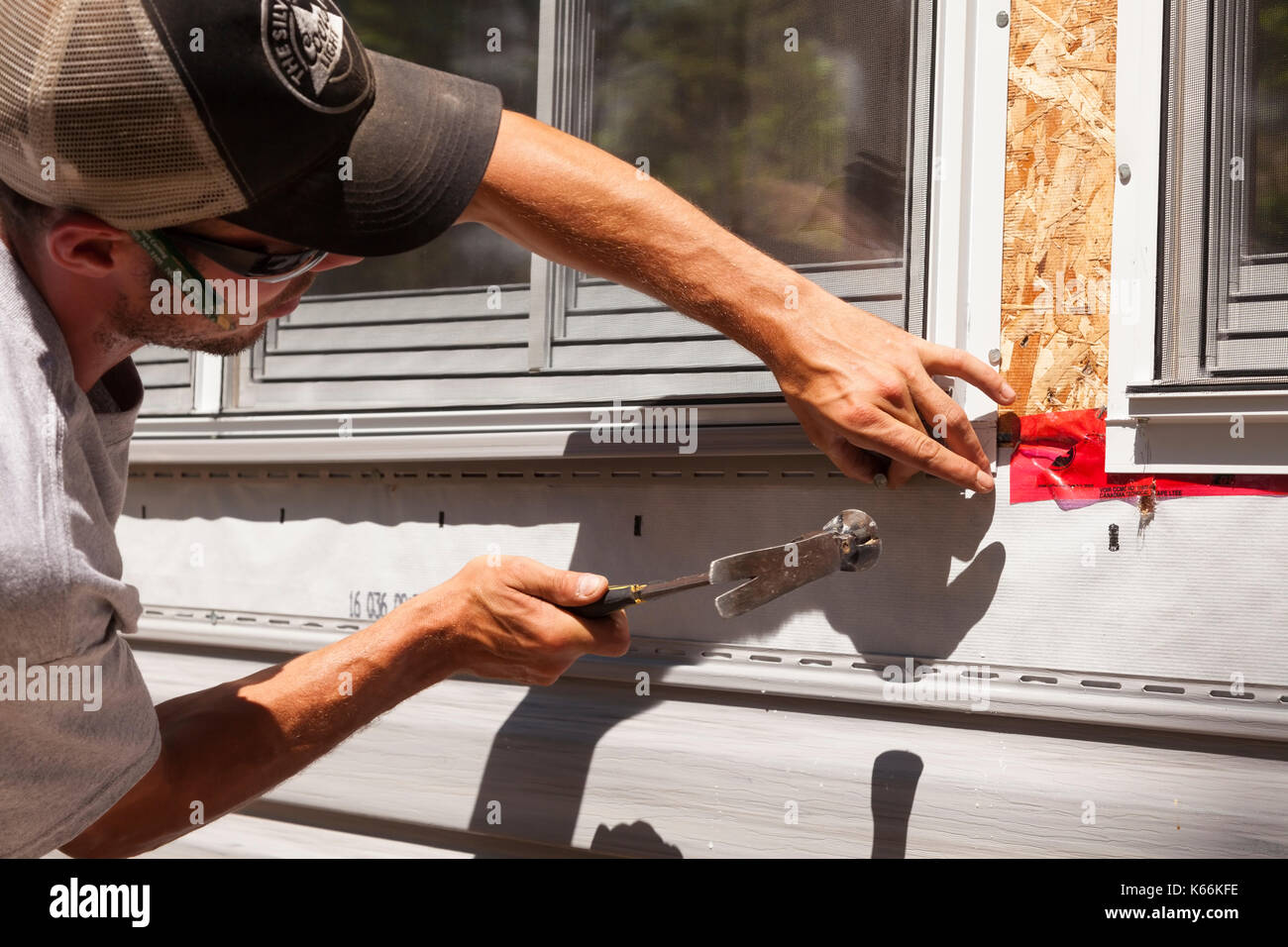 A construction worker hammering a nail to secure vinyl edging around a window in Ontario, Canada. Stock Photo