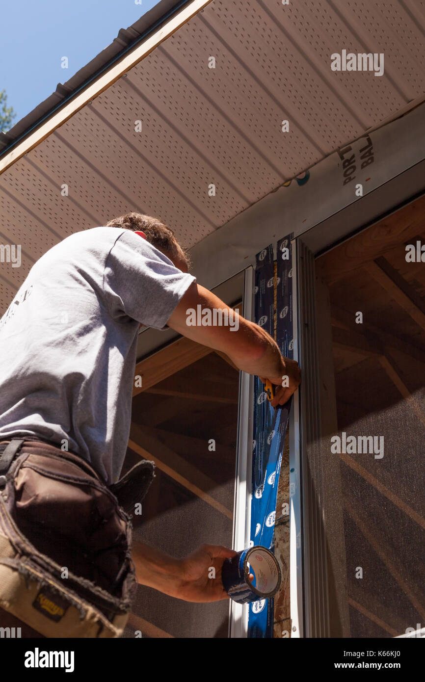 A construction worker applying sheathing tape or tuck tape to the outside wall of a new house in Ontario, Canada. Stock Photo