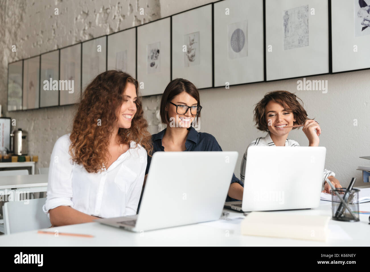 Three young happy women working by the table with laptop computers in co working office Stock Photo