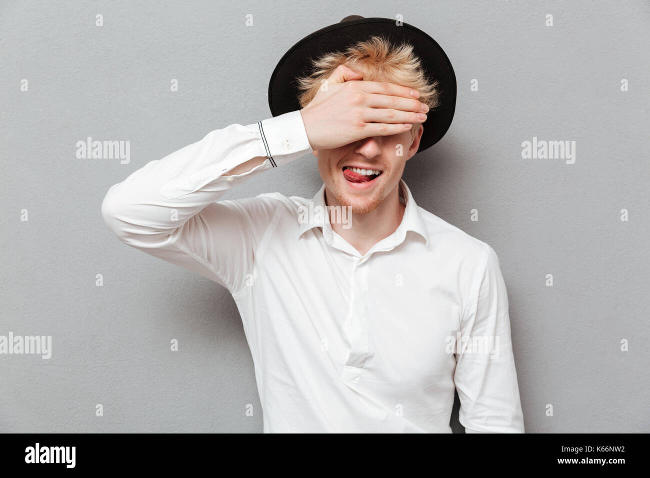 Photo of handsome cheerful young caucasian man covering eyes with hand ...