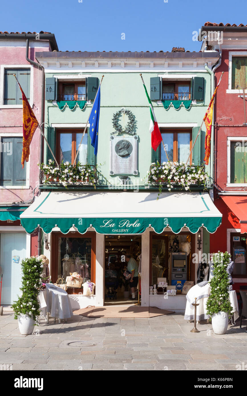 Picturesque exterior of La Perla Gallery, Burano, Venice, Veneto, Italy decorated with flags and flowers  with a 1911 memorial plaque to Doctor Lorenz Stock Photo