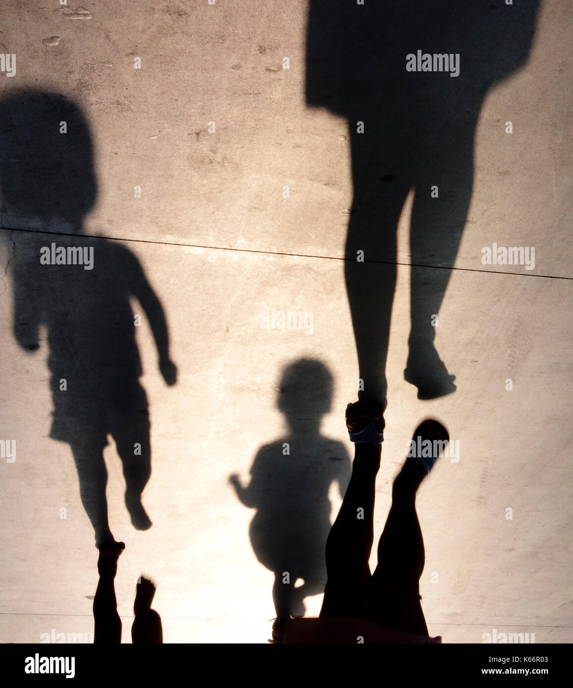 Blurry shadows of mother with two toddler kids running after her on summer promenade Stock Photo