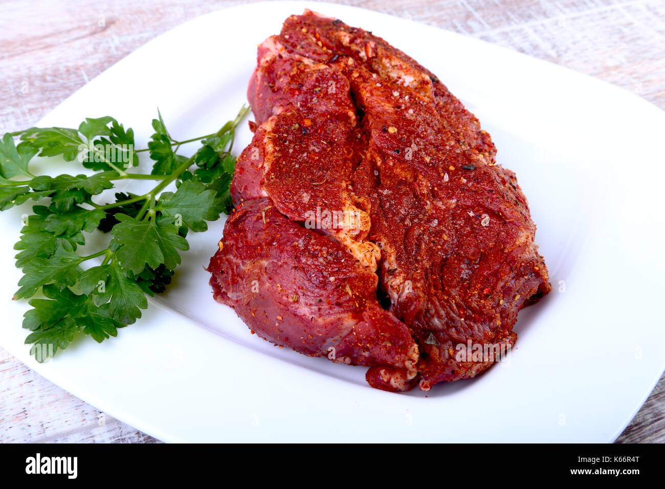 Raw beef steak with spices and Leaves of coriander on white plate. Ready for cooking Stock Photo