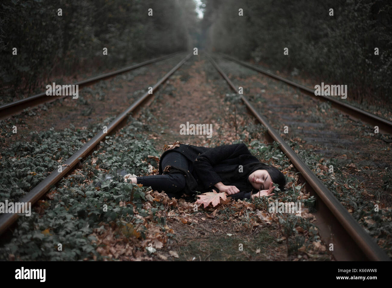 Caucasian woman laying on autumn leaves near train tracks in forest Stock Photo