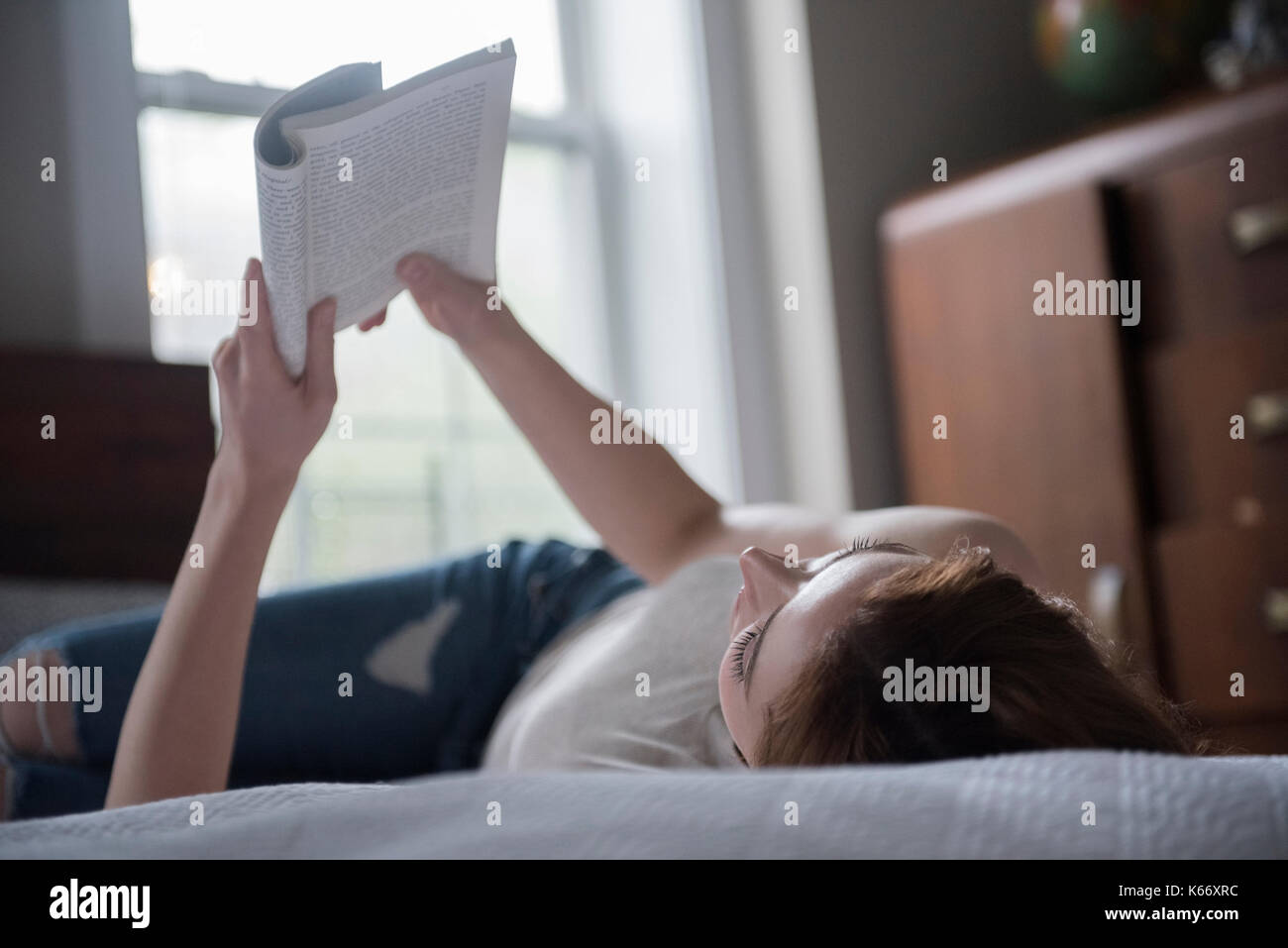 Caucasian woman laying on bed reading book Stock Photo