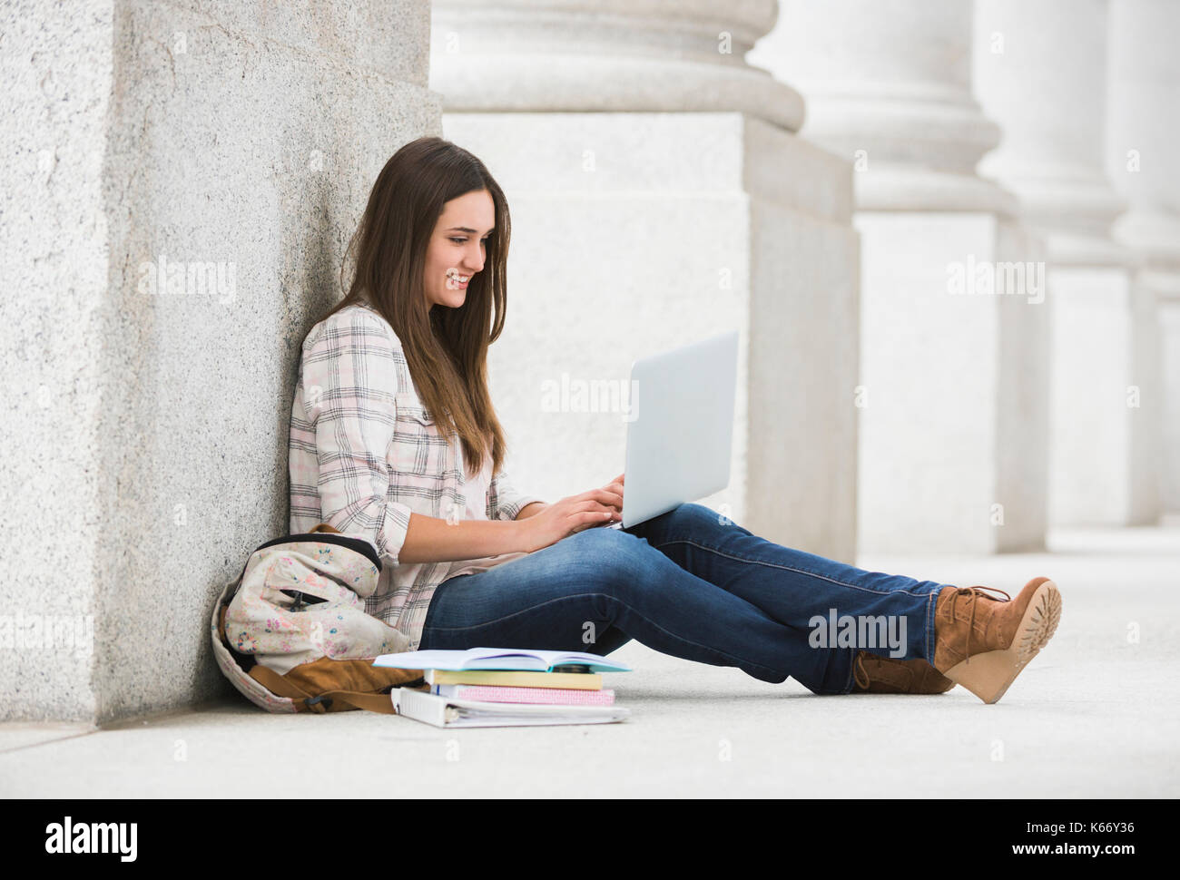 Caucasian woman leaning on pillar using laptop Stock Photo
