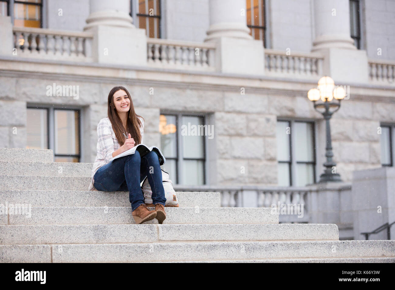 Smiling Caucasian woman sitting on staircase holding notebook Stock Photo