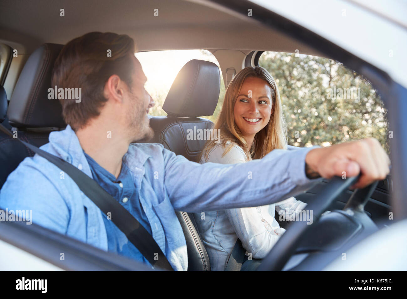 Young couple going on holiday in a car smiling to each other Stock Photo
