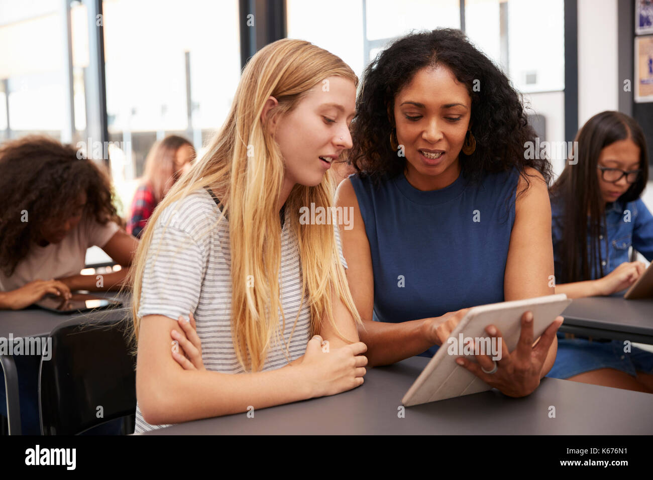 Teacher helps blonde teenage schoolgirl with tablet computer Stock Photo