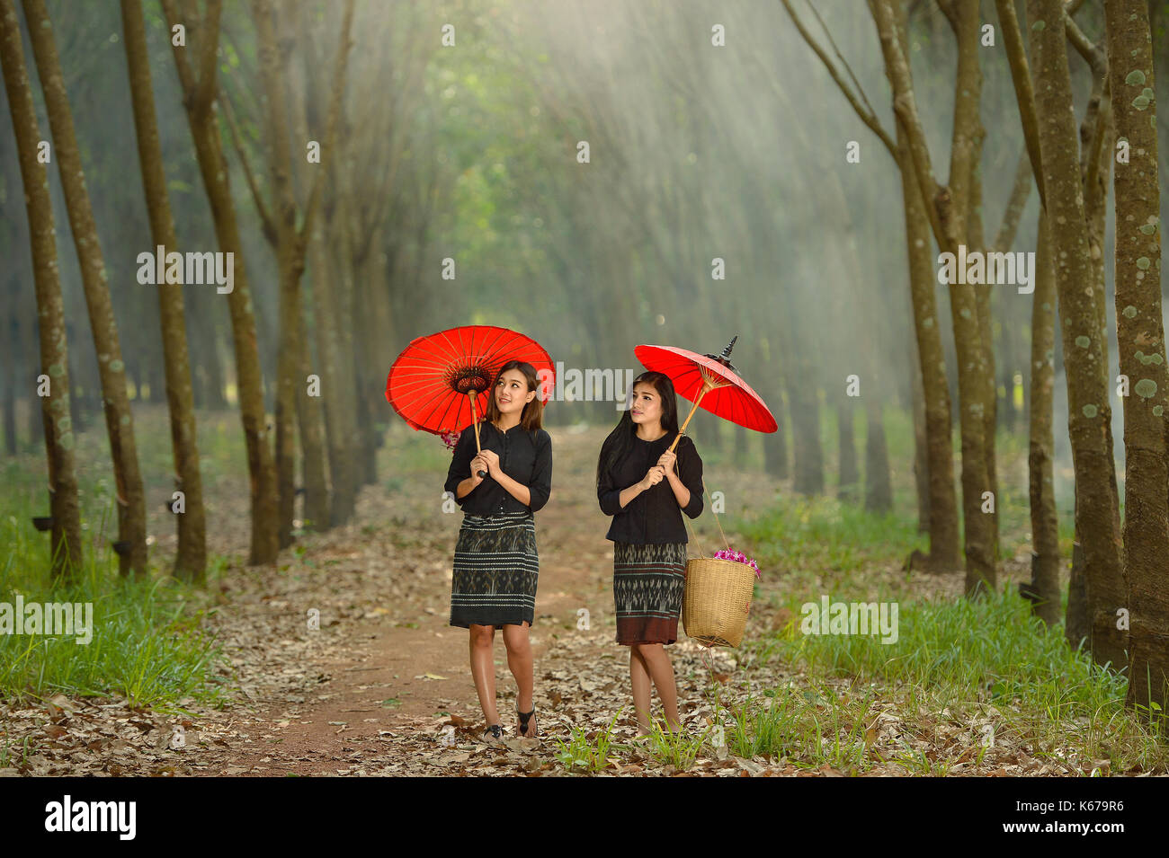 Two women walking along rural footpath with parasols, Thailand Stock Photo