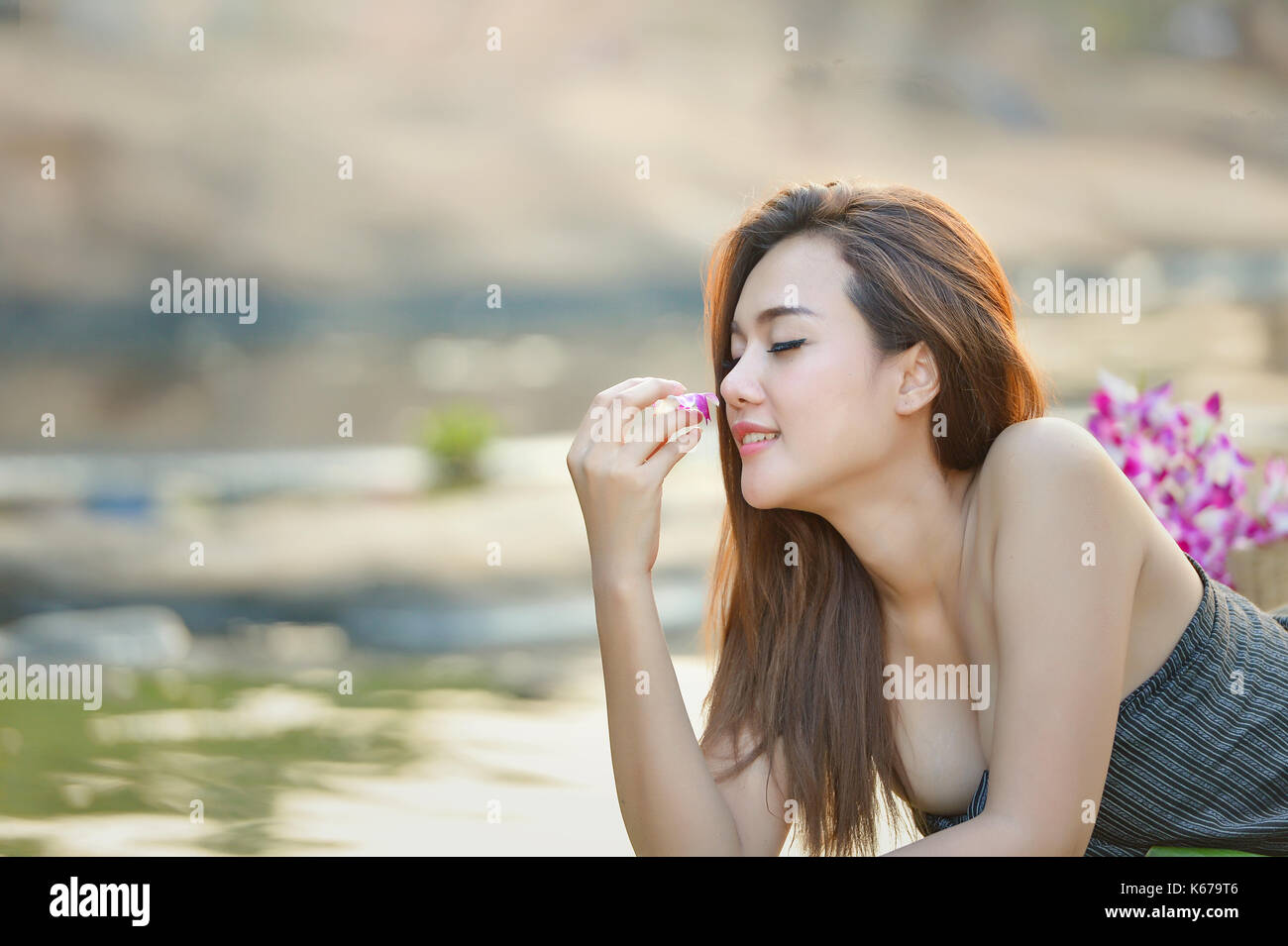 Woman lying by a river smelling a flower, Thailand Stock Photo