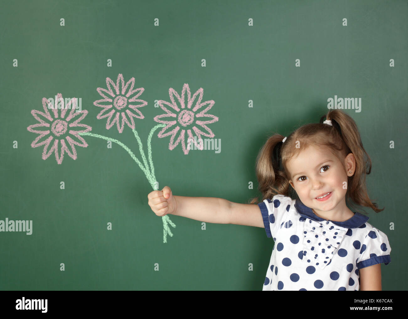 Smiling child hold drawn flowers near school blackboard Stock Photo