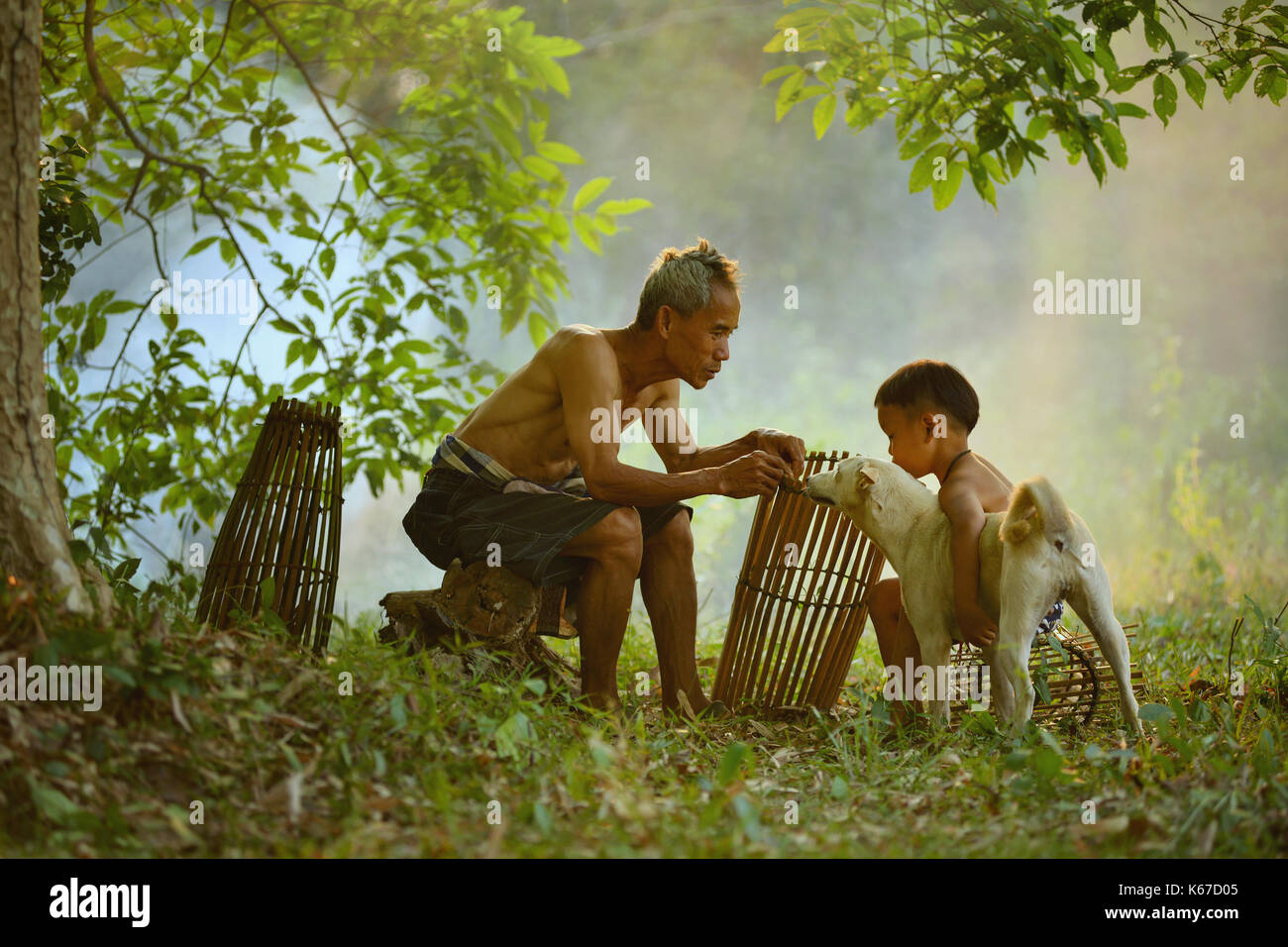 Grandfather and grandson sitting in forest playing with a dog, Thailand Stock Photo