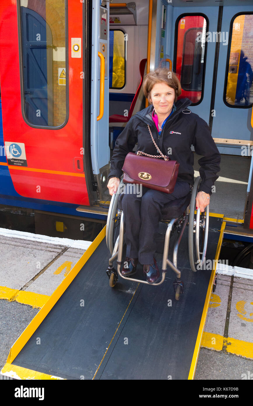 Wheel chair user / person in a wheelchair departing / leaving / alighting from a train carriage onto a platform using a ramp provided at the station. Stock Photo