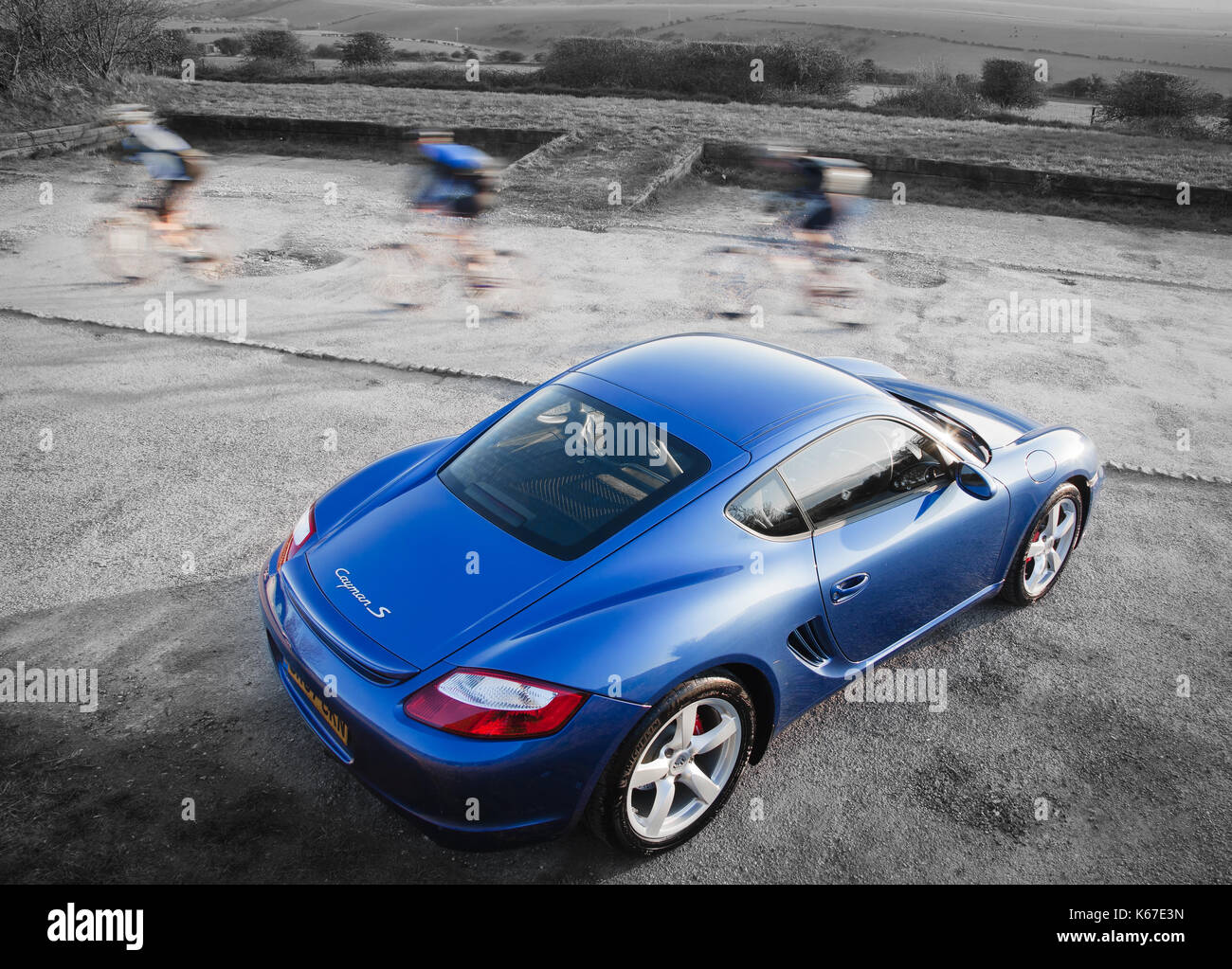 Porsche Cayman S 2007 in Cobalt Blue with cyclist whizzing past Stock Photo
