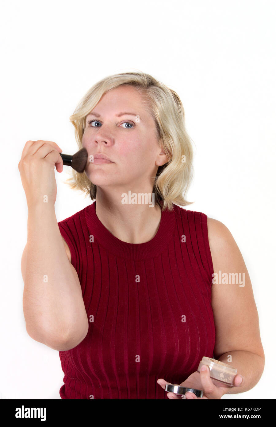 woman with red face puts on makeup powder from a case in the studio Stock Photo